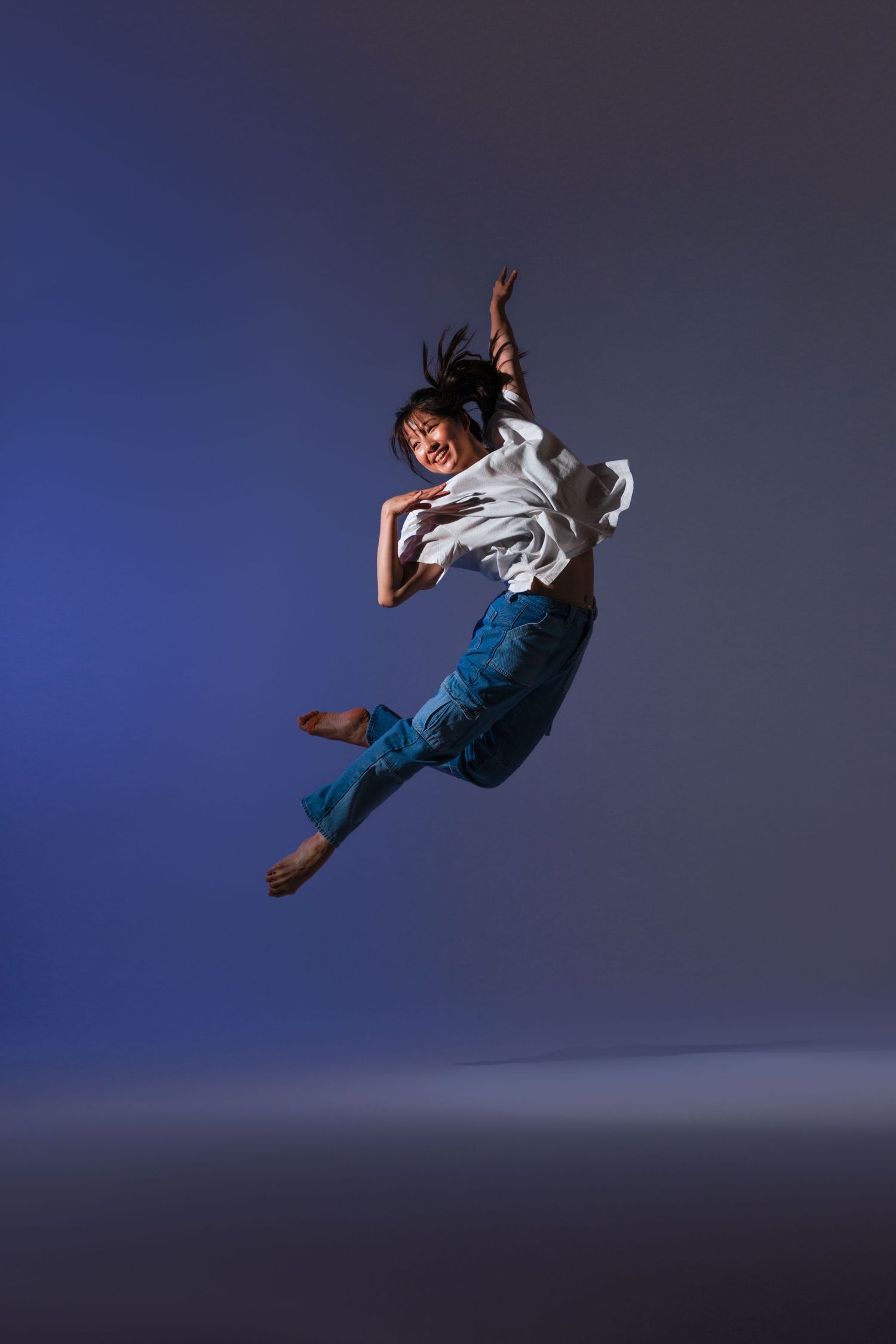 Dynamic dance movement captured mid-leap with flowing white top and jeans.