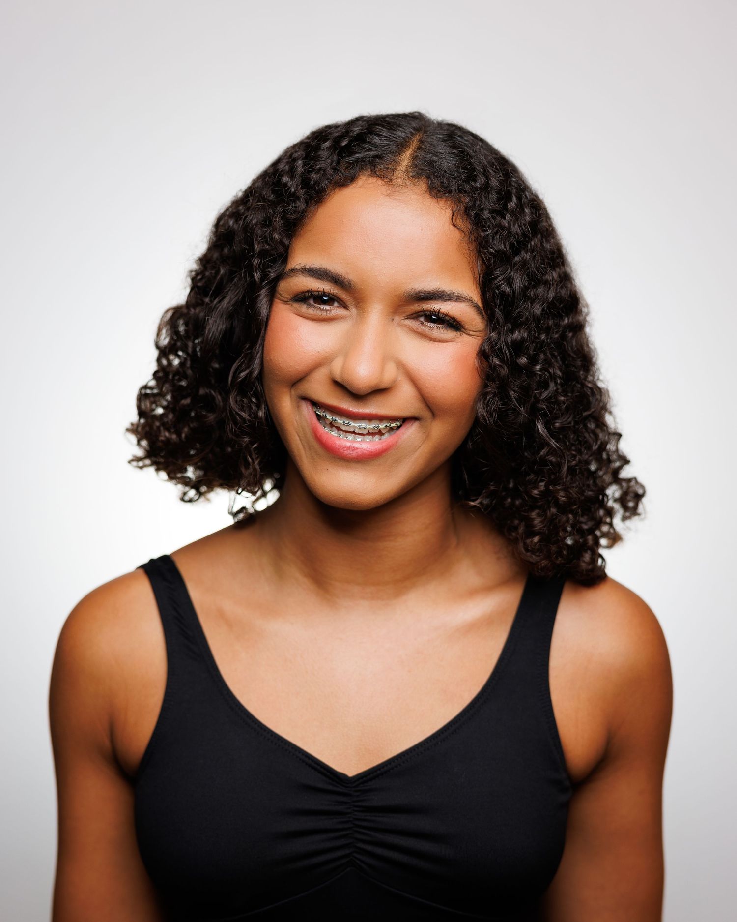 Dance portrait featuring natural curly hair and warm smile against white backdrop.
