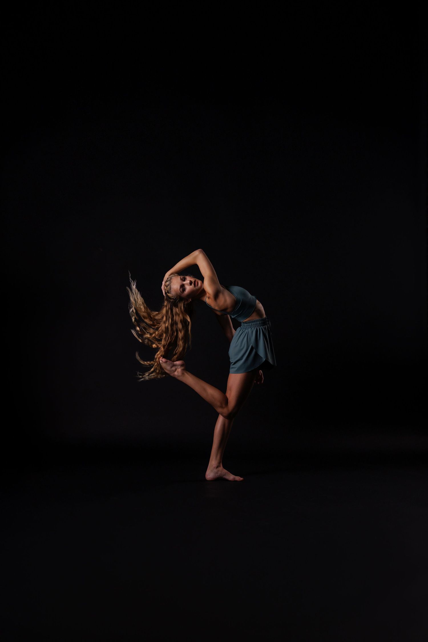 Dancer performs expressive backbend with flowing hair against dark backdrop.