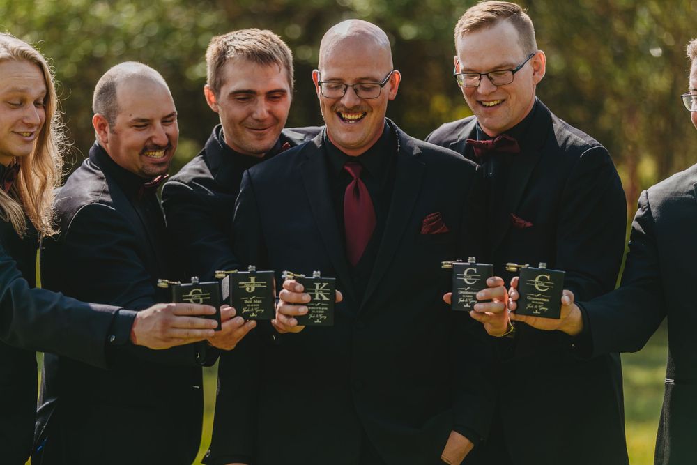 Group photo of wedding party members holding drinks and smiling outdoors.