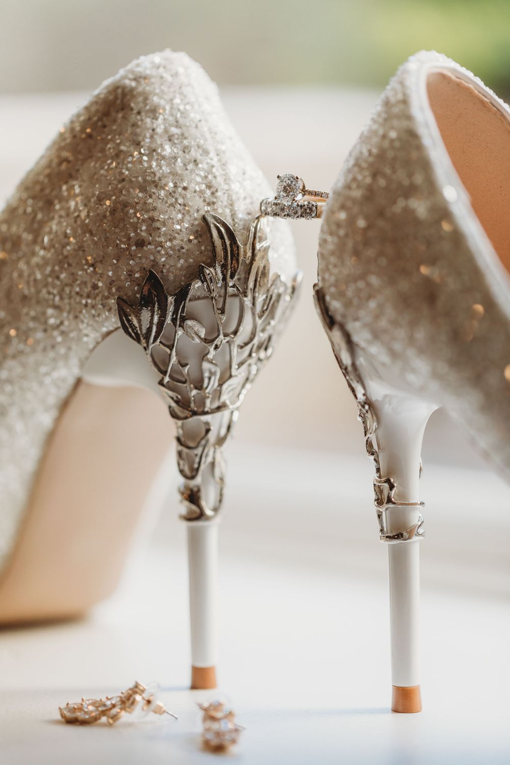 Sparkly white wedding heels with ornate silver designs displayed with an engagement ring.