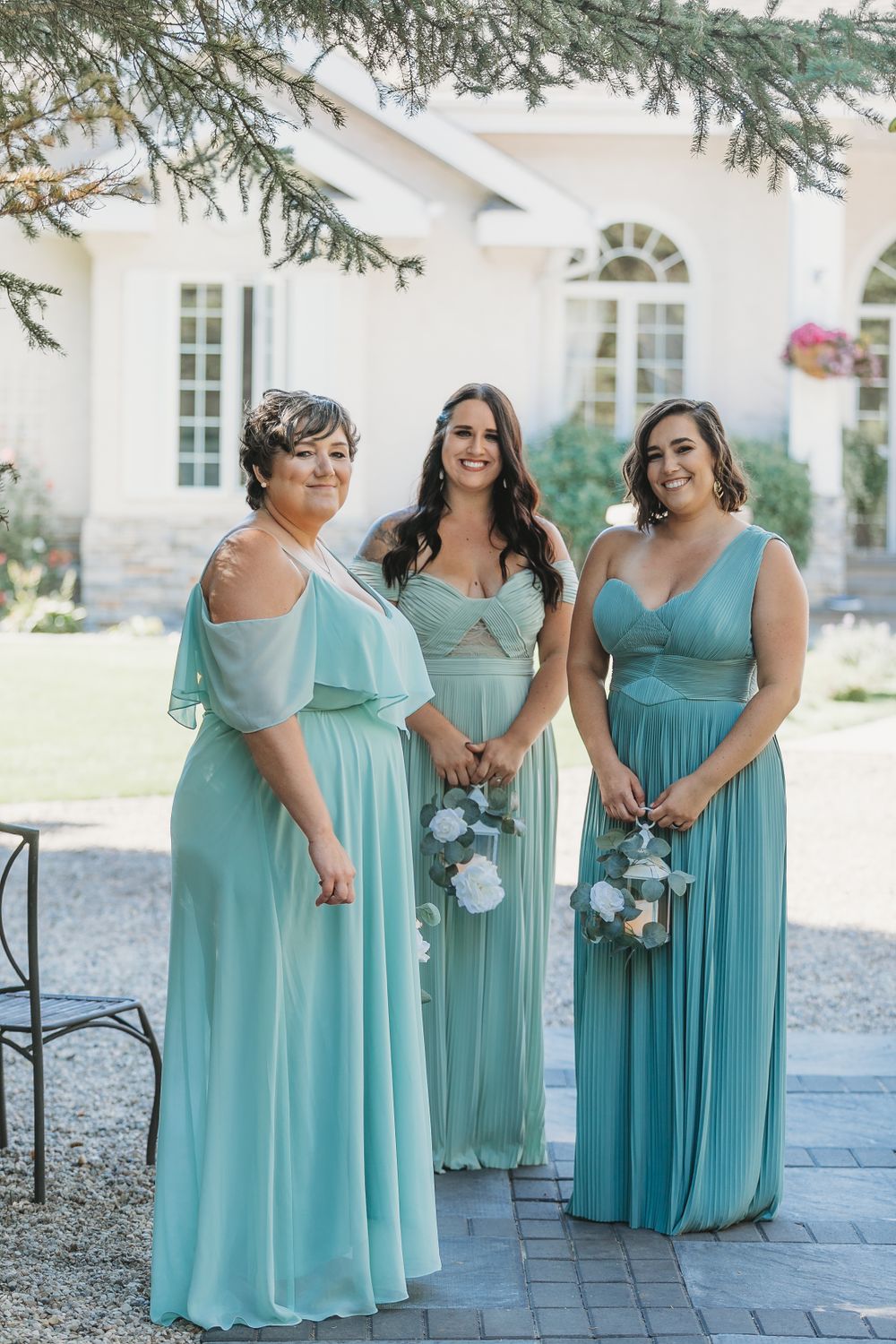 Three bridesmaids in matching seafoam blue dresses pose with bouquets outside a white building.