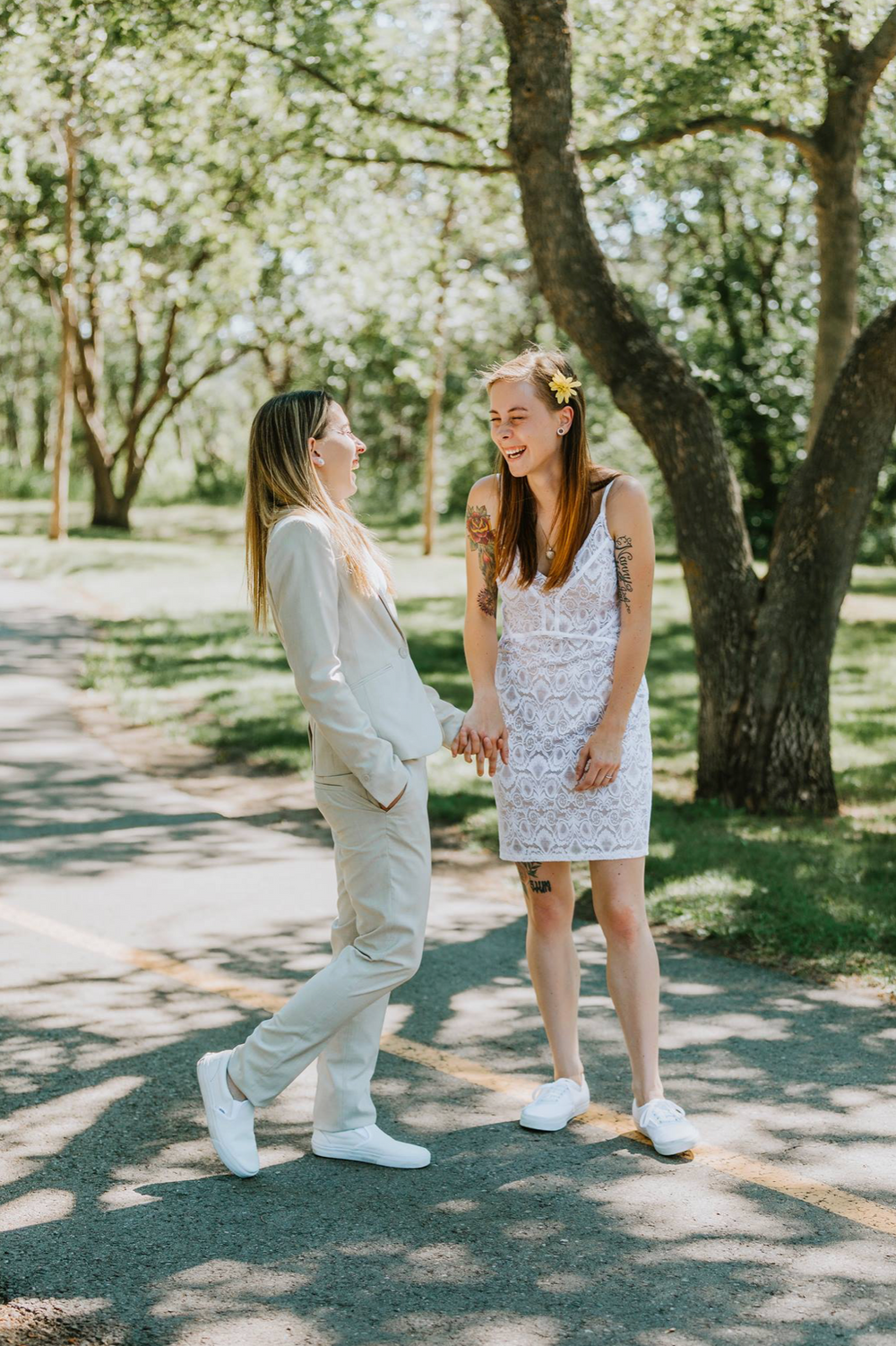 Casual outdoor wedding portrait of couple laughing in sunlit garden path.