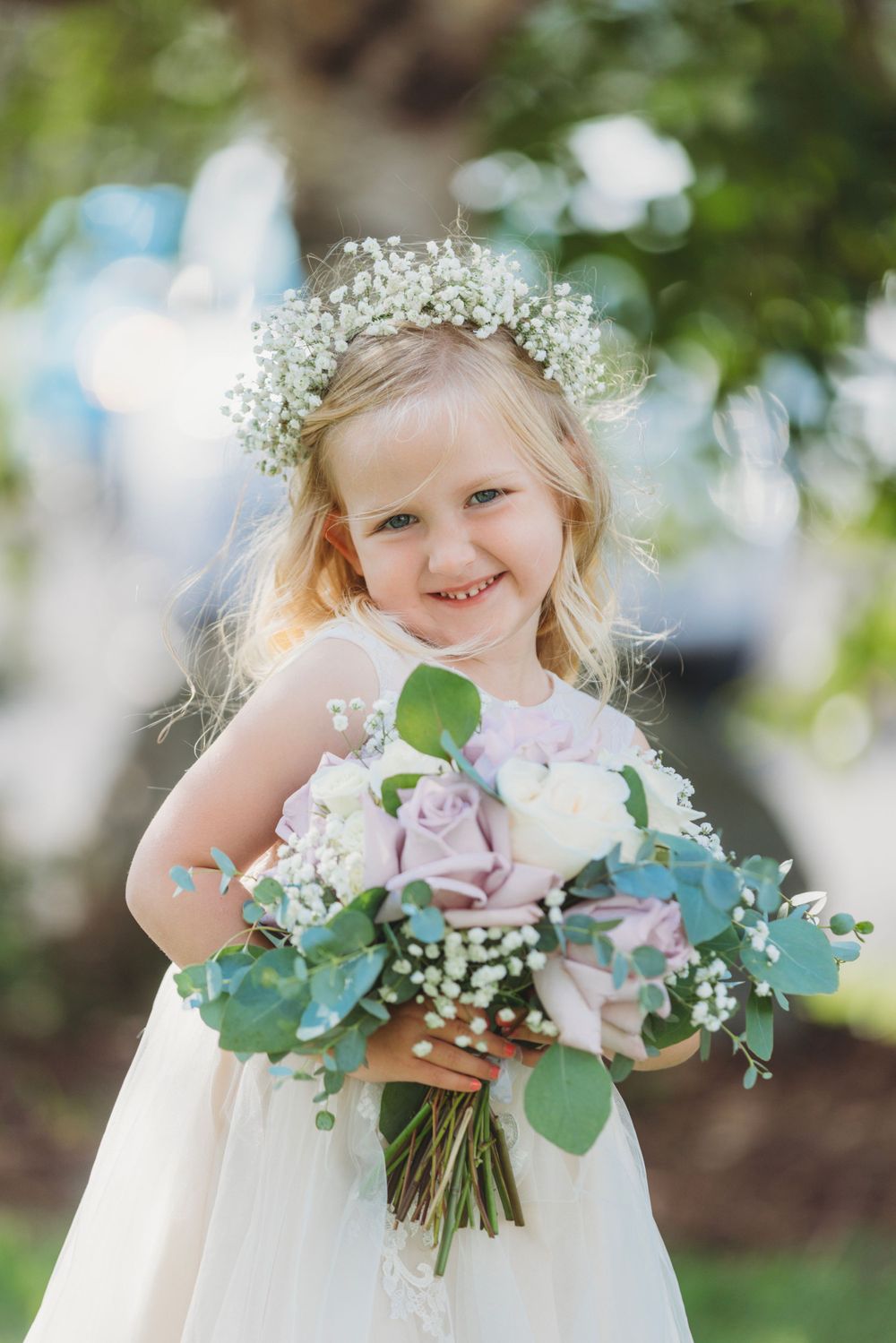 Young flower girl wearing white dress and floral crown holding pastel bouquet.