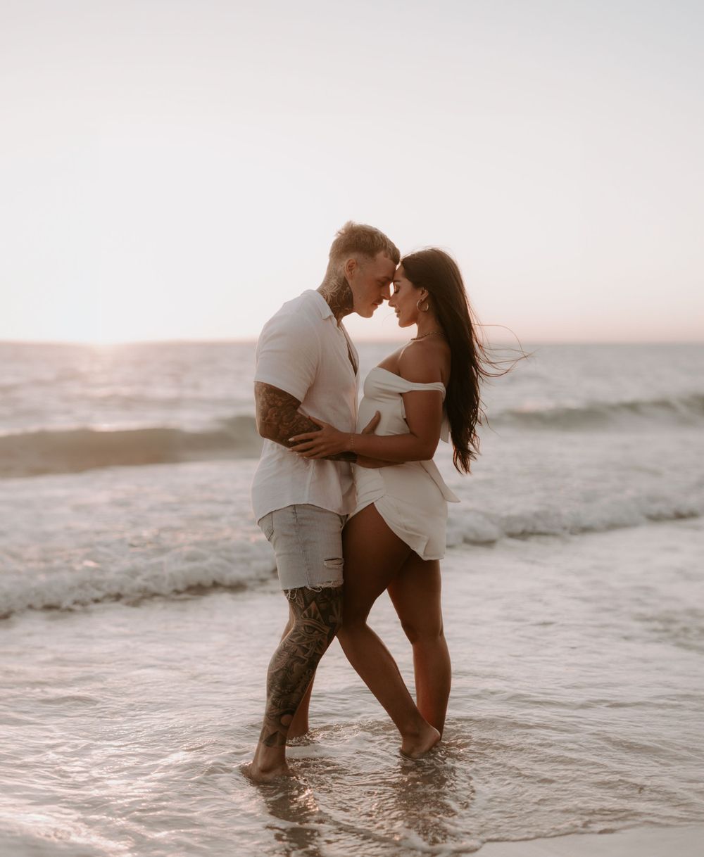 Couple embracing in shallow ocean water during sunset.