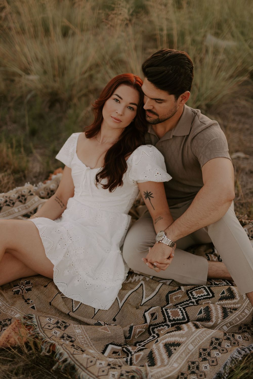 Romantic couple sitting on a patterned blanket in a natural outdoor setting during a golden hour photoshoot.