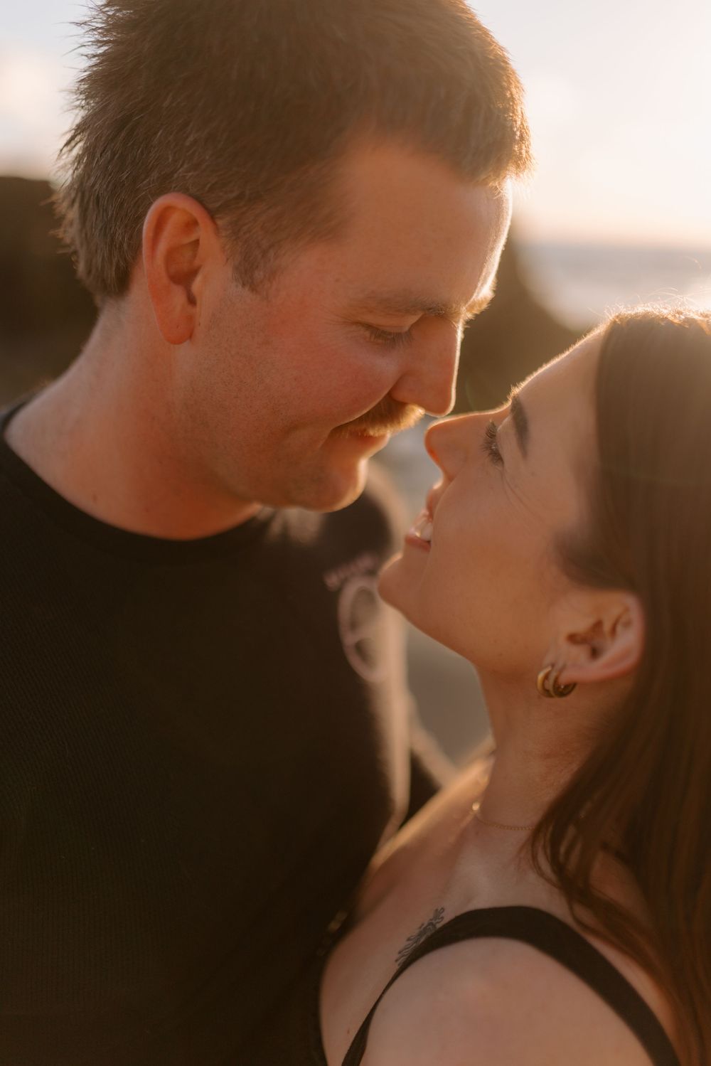 A romantic couple sharing an intimate moment at sunset with golden light illuminating their faces.