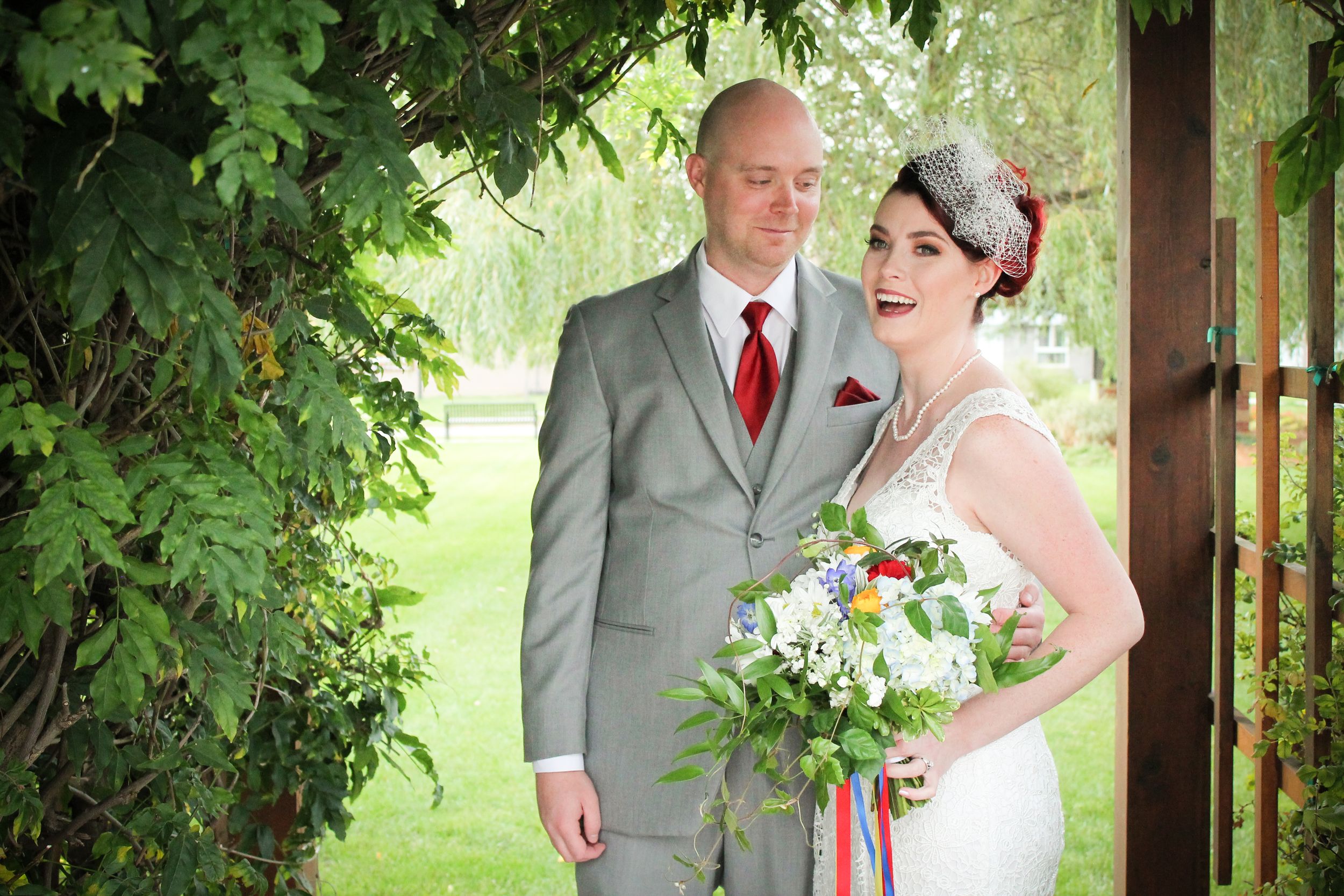 A vintage-styled wedding couple poses under a lush green garden archway.