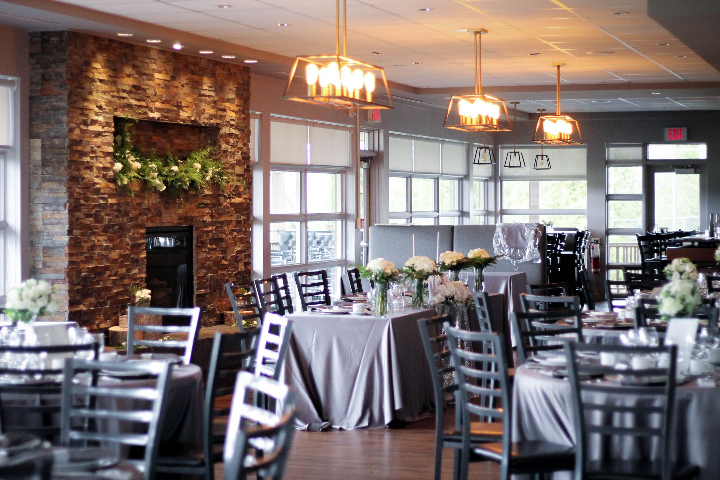 Modern restaurant interior with stone walls, chandeliers, and elegant table settings.