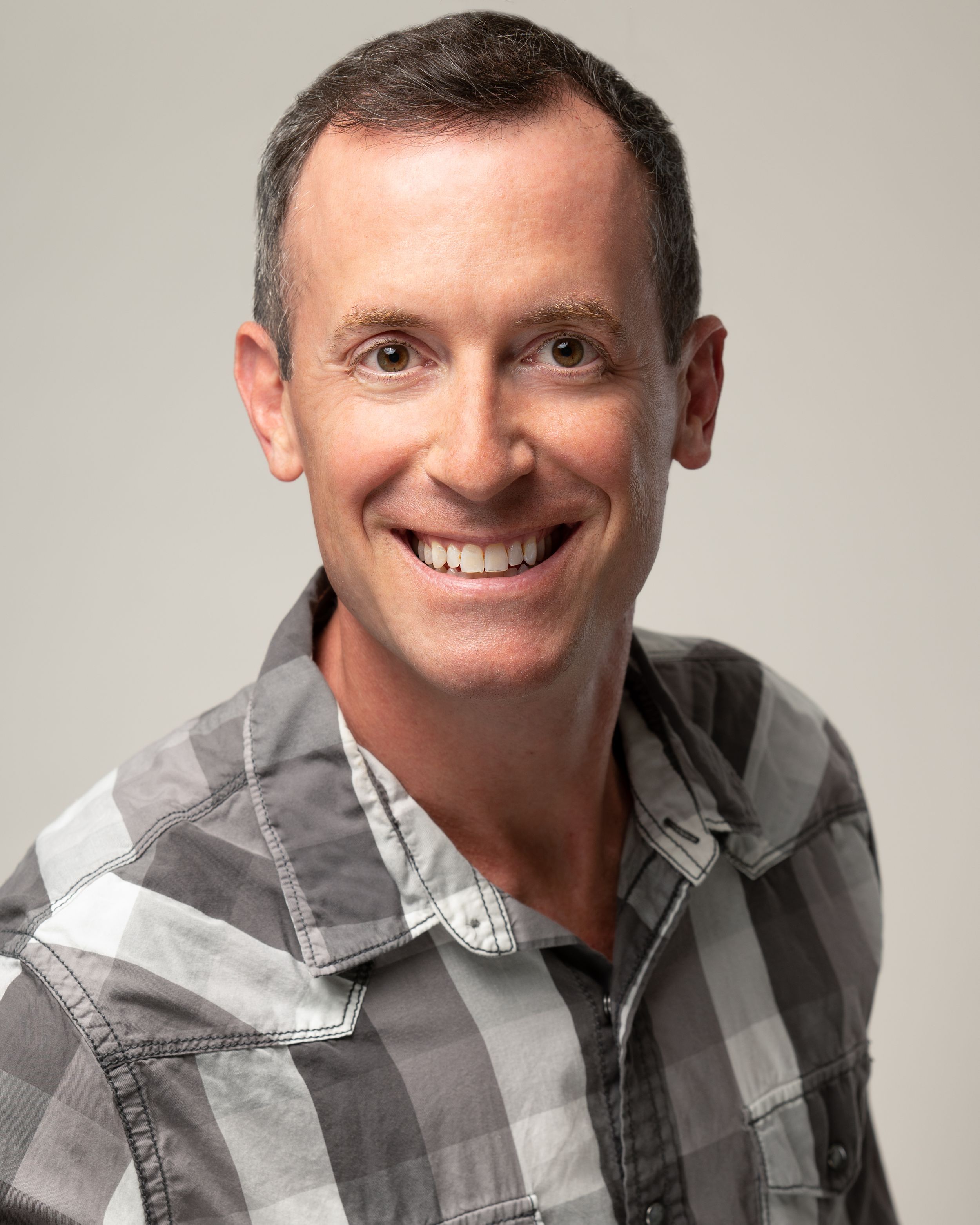 Professional headshot of a wedding photographer in South Jersey wearing a gray and white plaid button-down shirt against a light background.