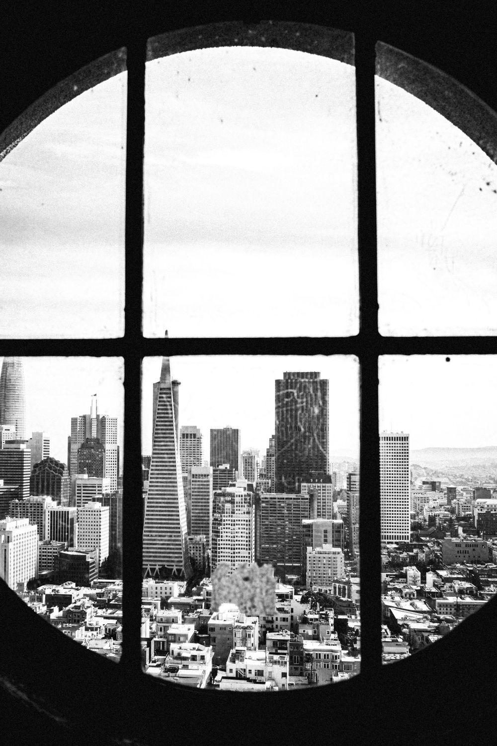 Dramatic black and white cityscape viewed through curved window showing urban skyscrapers.
