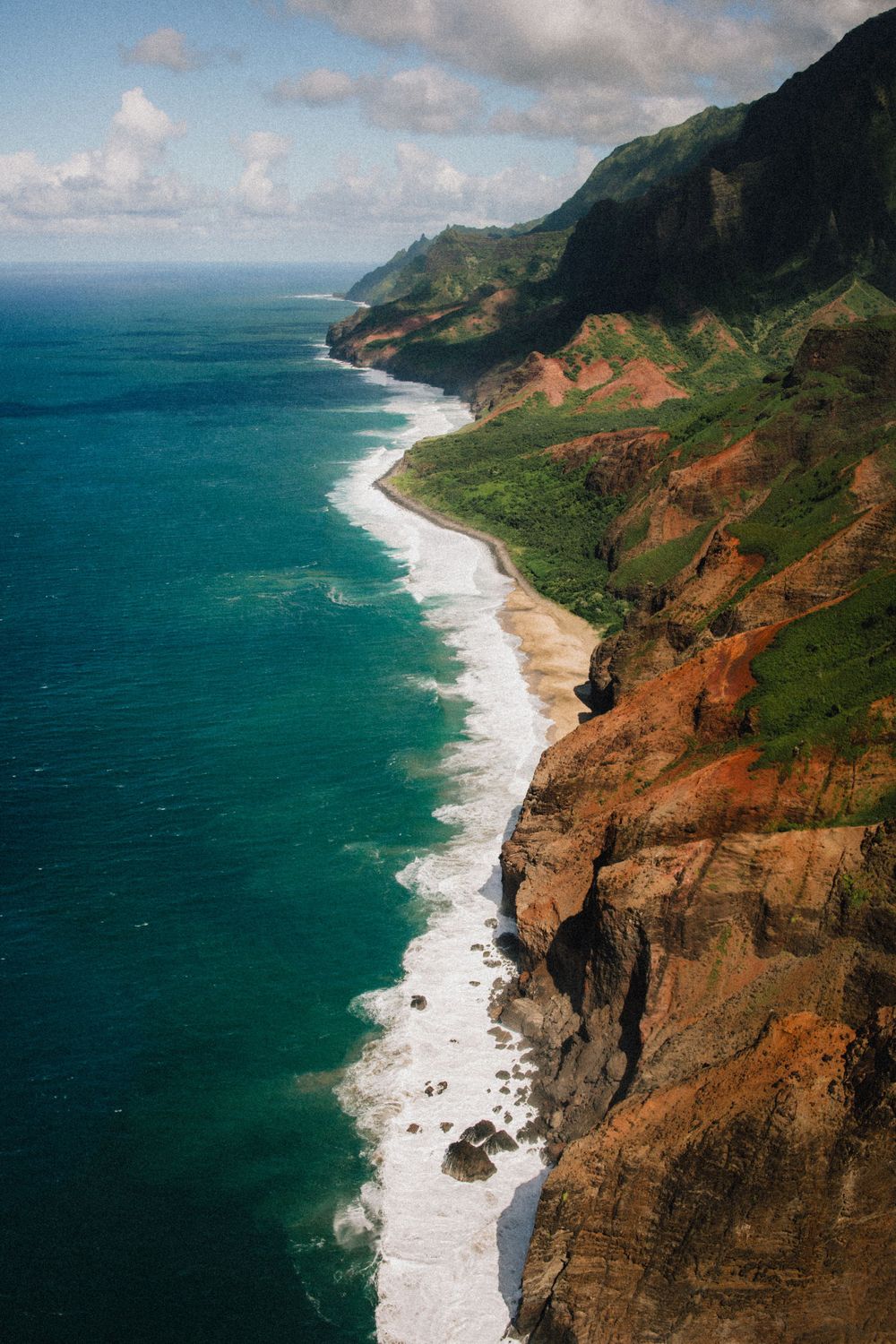 Aerial view of dramatic Na Pali coast in Kauai with turquoise waters meeting rugged cliffs.
