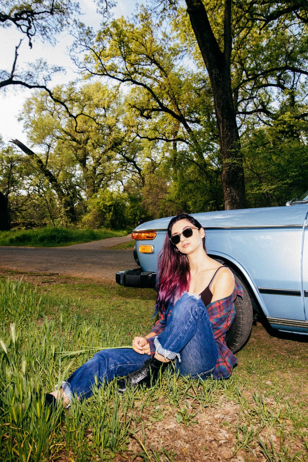 Retro car photoshoot in natural outdoor setting with greenery and casual fashion styling.