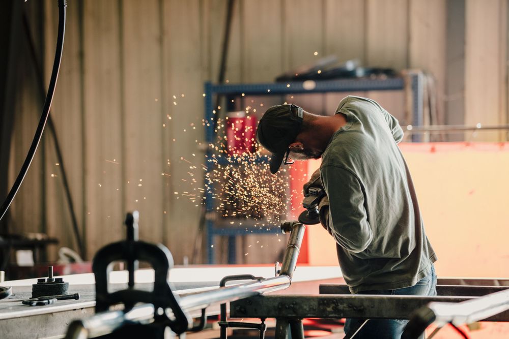 Welder in green shirt creating sparks while working in a workshop setting.