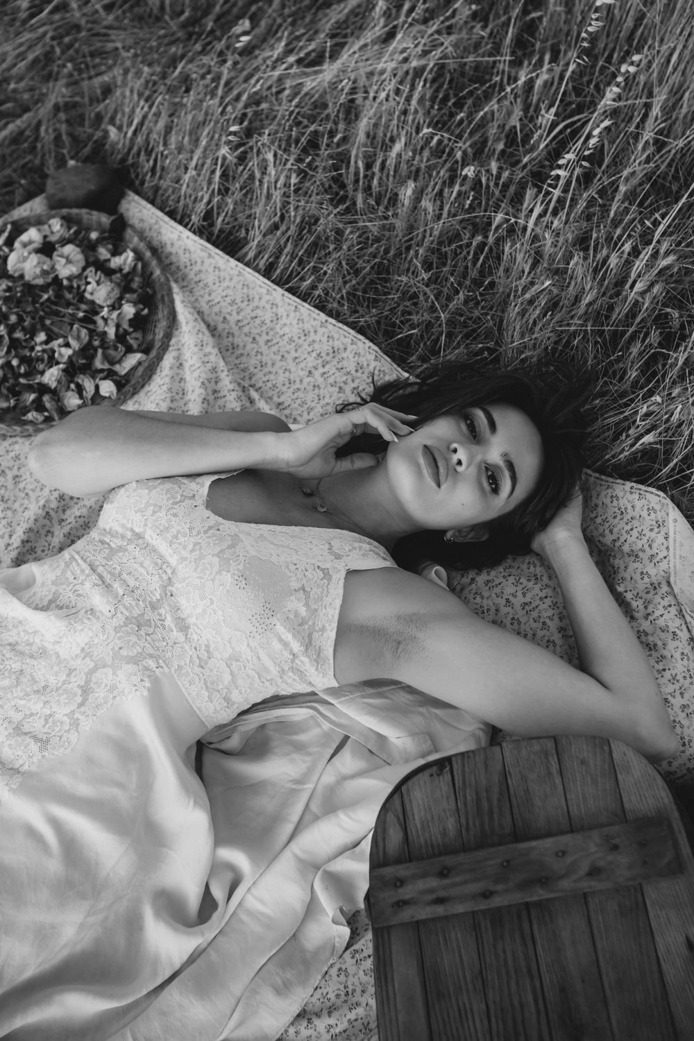 Dreamy black and white portrait of figure lying in tall grass wearing light flowing dress.