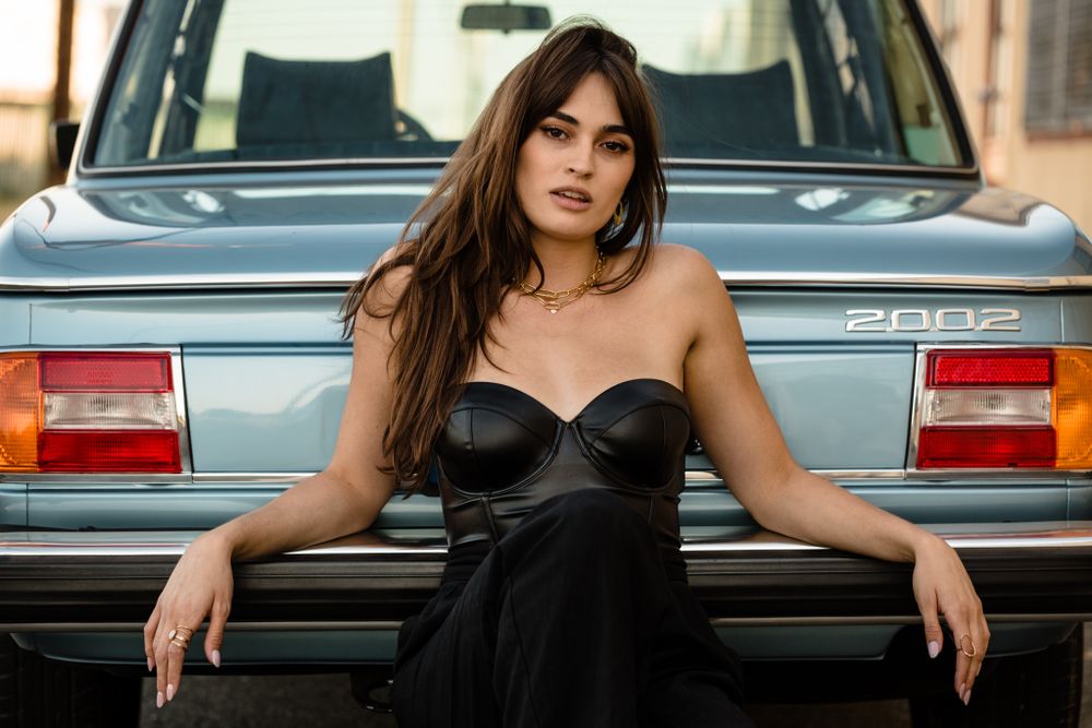 Portrait against vintage car featuring elegant black dress and natural lighting.