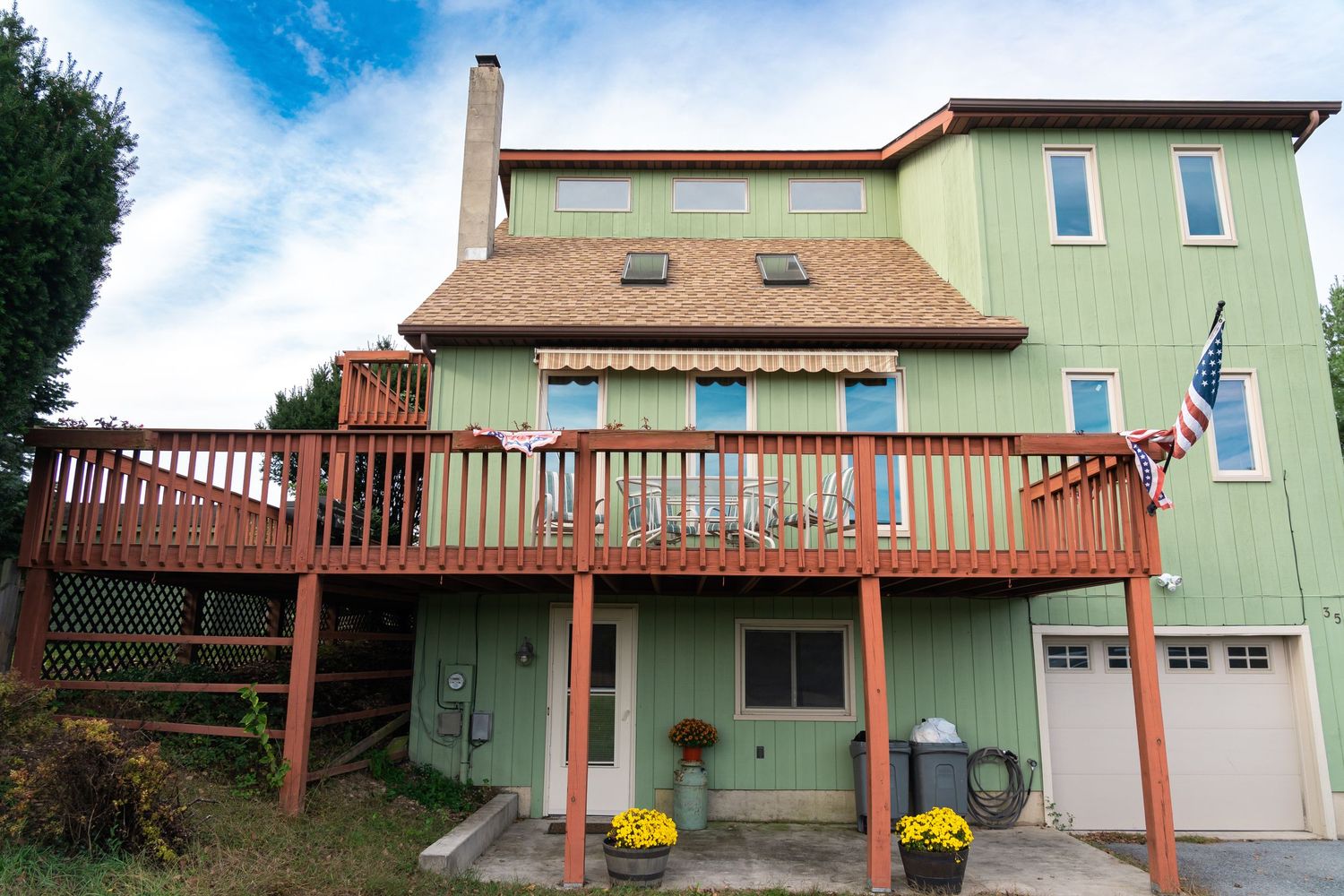 Light green house exterior with wooden deck and railing under blue sky.