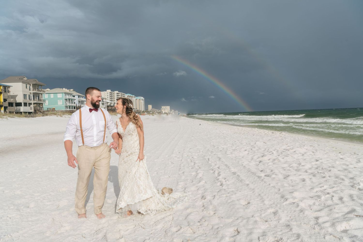 Stormy beach scene with rainbow over ocean and white sand.
