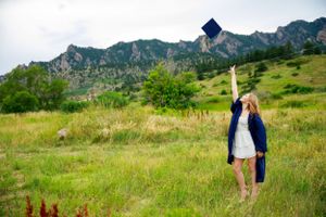 Graduate tosses cap in celebration with mountain backdrop.