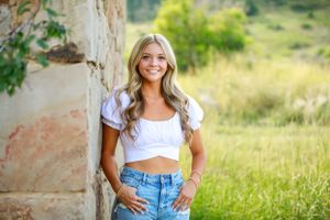 Person in crop top and jeans poses against rustic stone wall in countryside setting.
