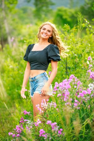 Person in puff sleeve top poses among pink wildflowers in mountain meadow.