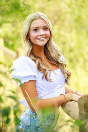 Person in white peasant top and jeans poses in sunny meadow setting.