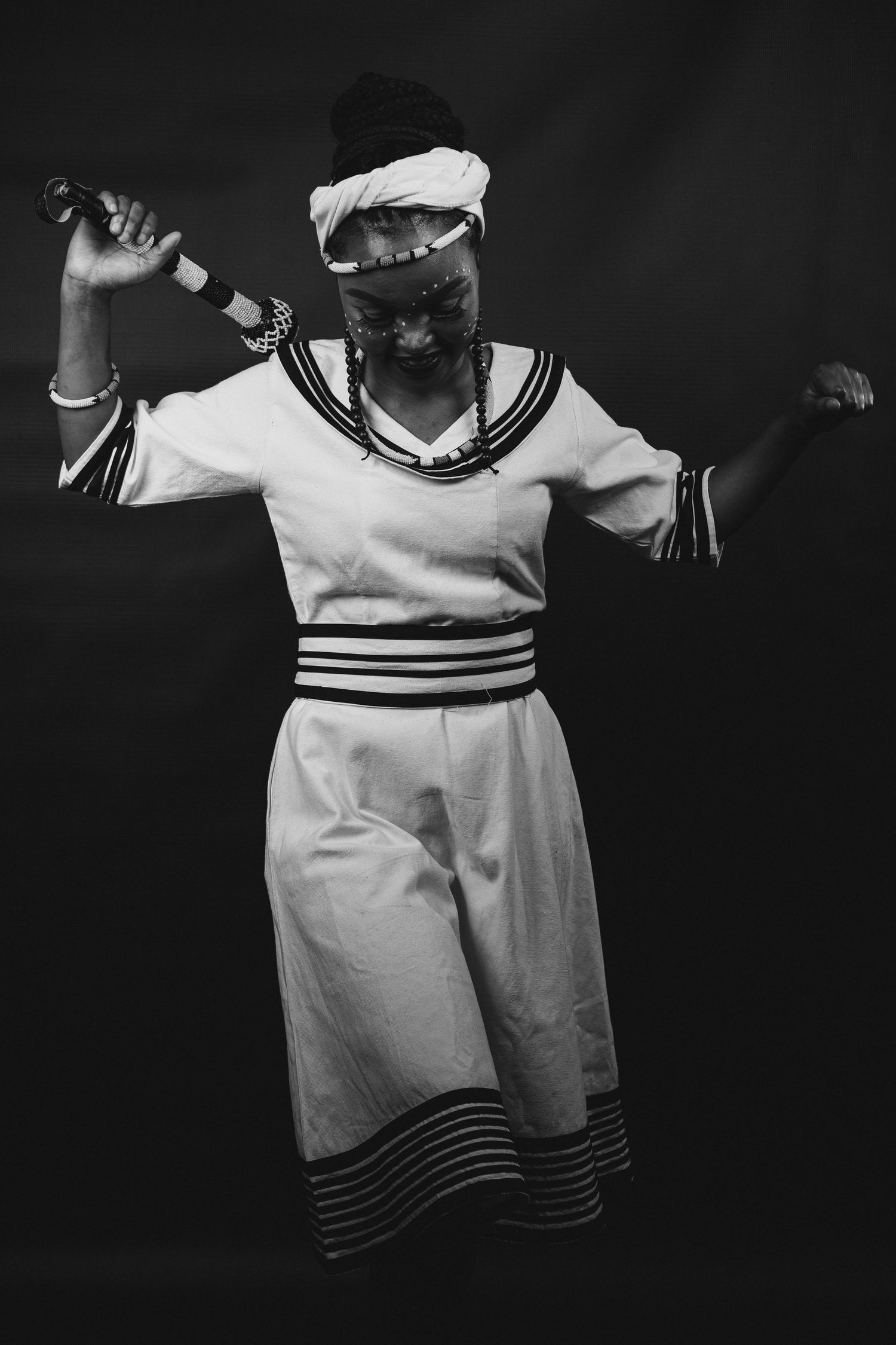 Studio shoot, of a lady celebrating her Xhosa heritage, dancing with her rode, showing excitement about her culture, black and white photo.