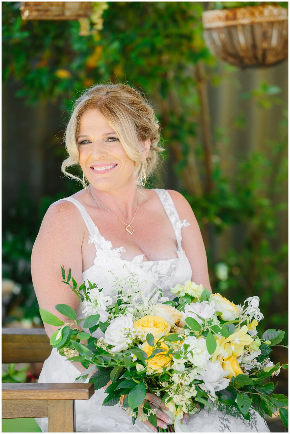 Bride with bouquet of yellow and white flowers posed in garden setting.