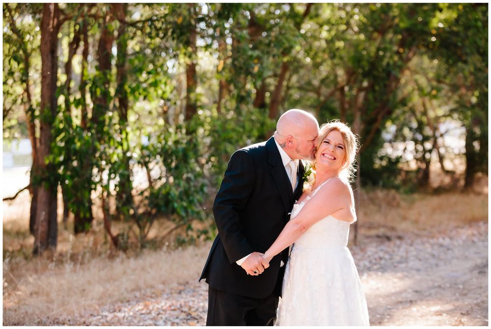 Couple shares romantic moment in sunlit wooded area during wedding photoshoot.