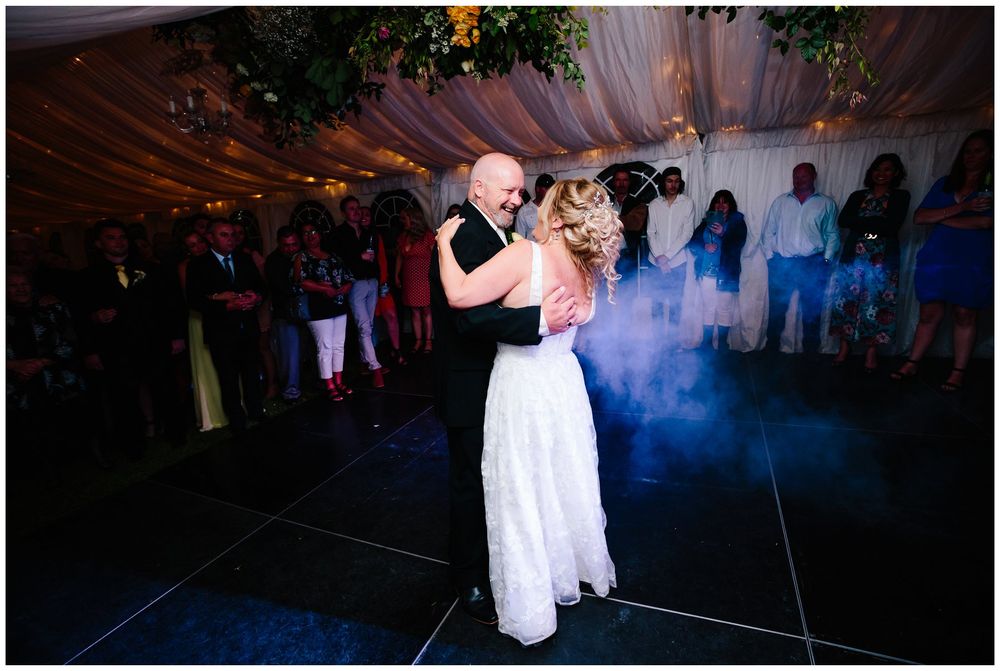 Couple's first dance in a decorated venue with atmospheric smoke and lighting.