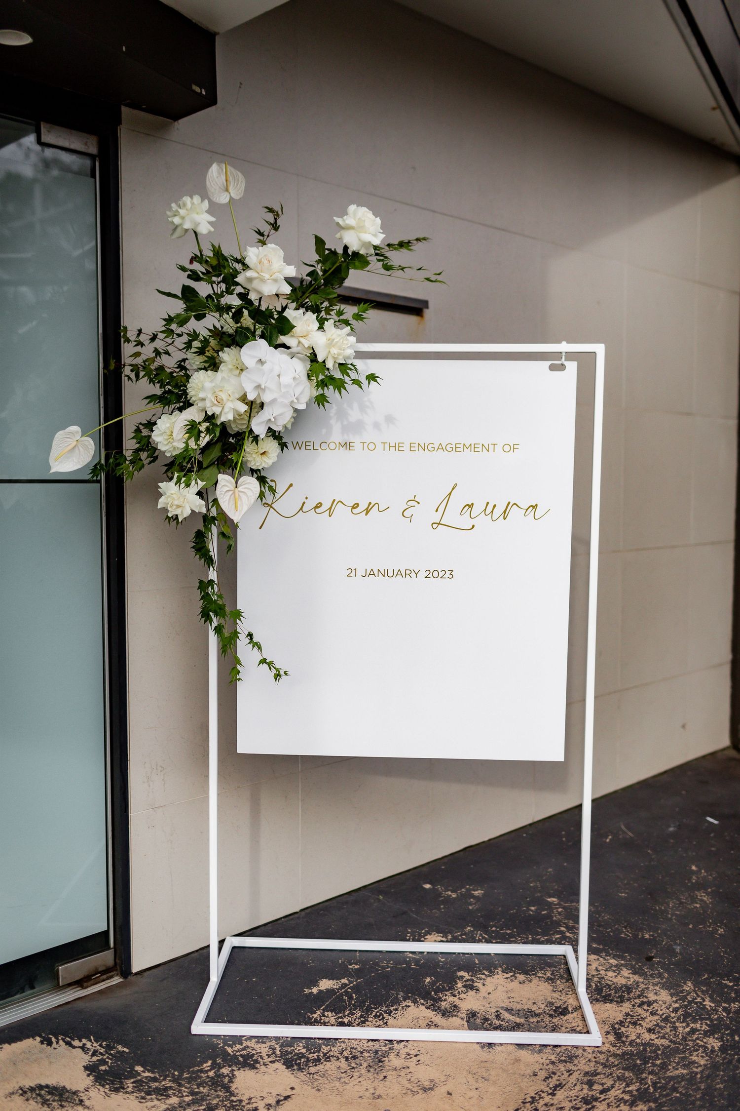 Wedding welcome sign with white and gold text, adorned with white floral arrangements.