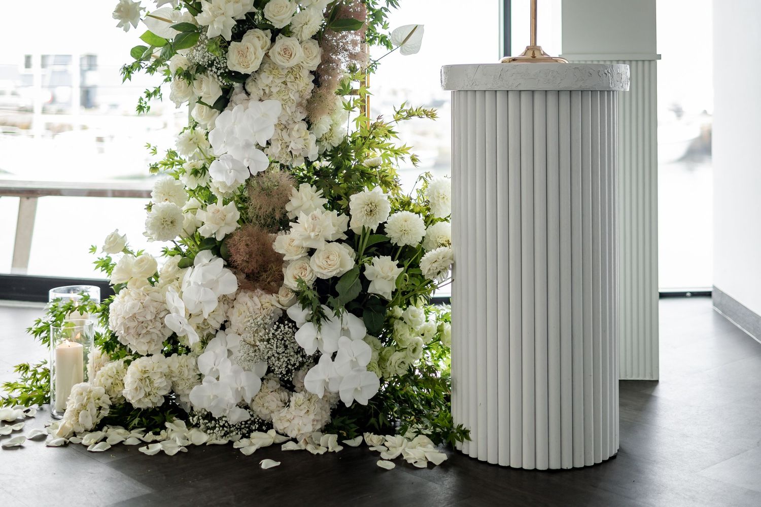 Dramatic white floral arrangement cascading alongside modern white pedestal.