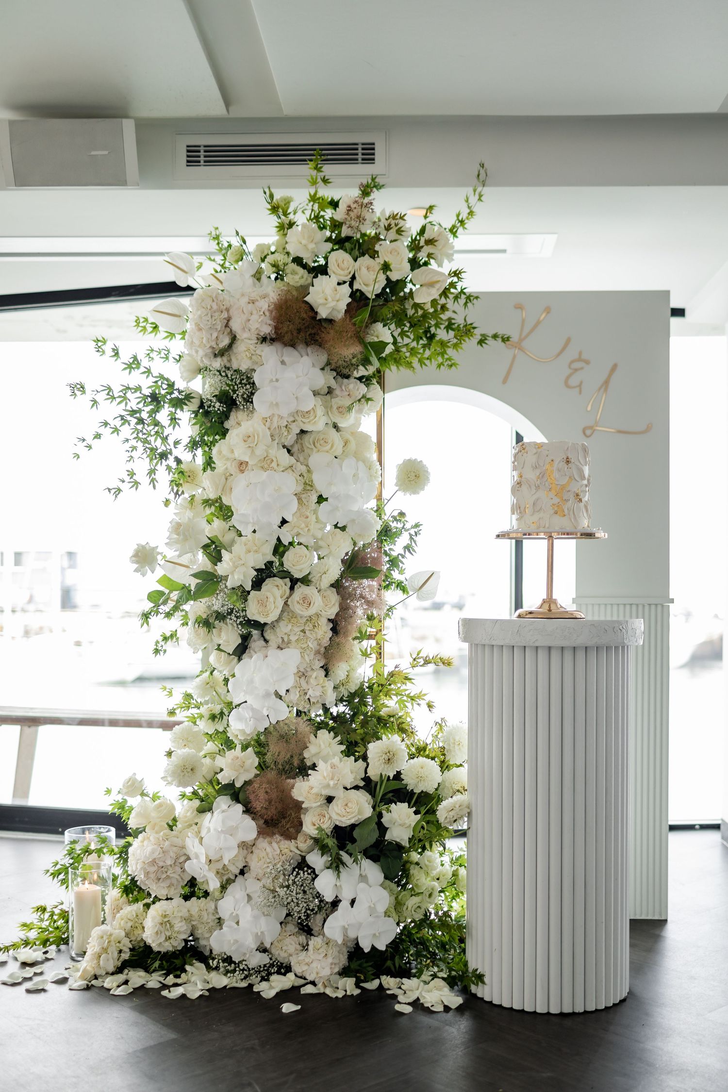 Towering white floral installation with greenery next to elegant wedding cake display.
