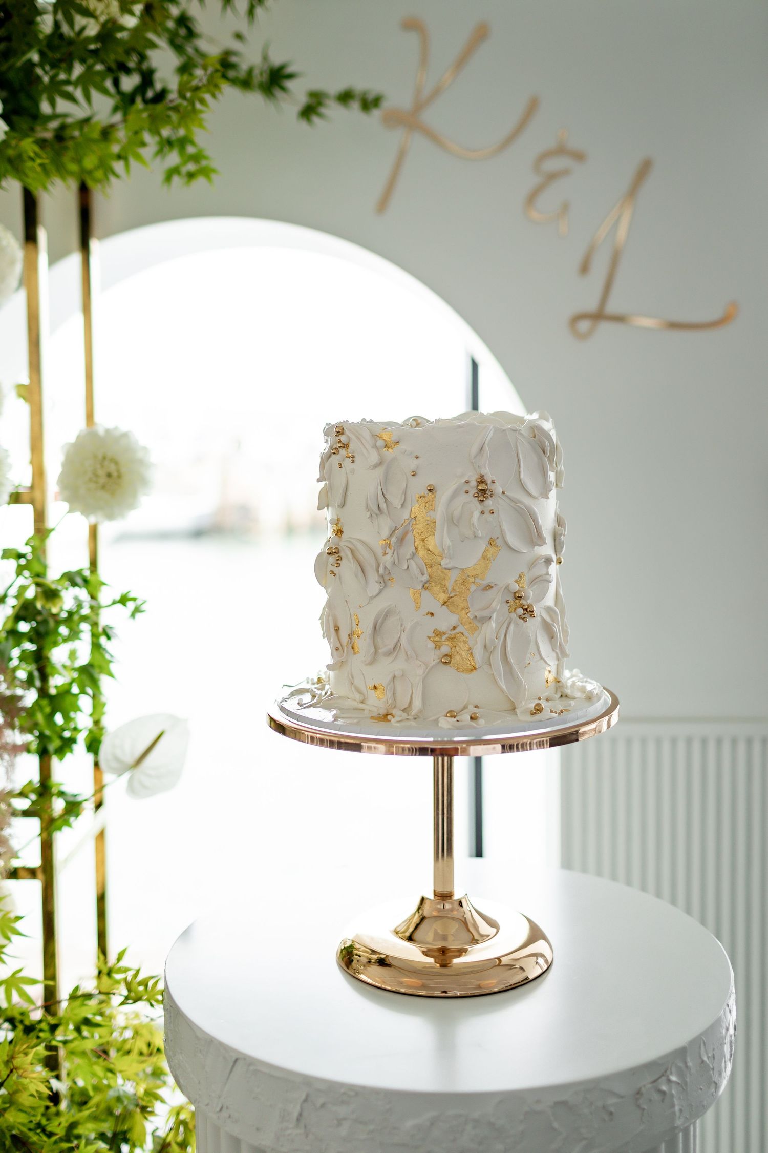 Modern white and gold wedding cake on rose gold stand with textured detailing.