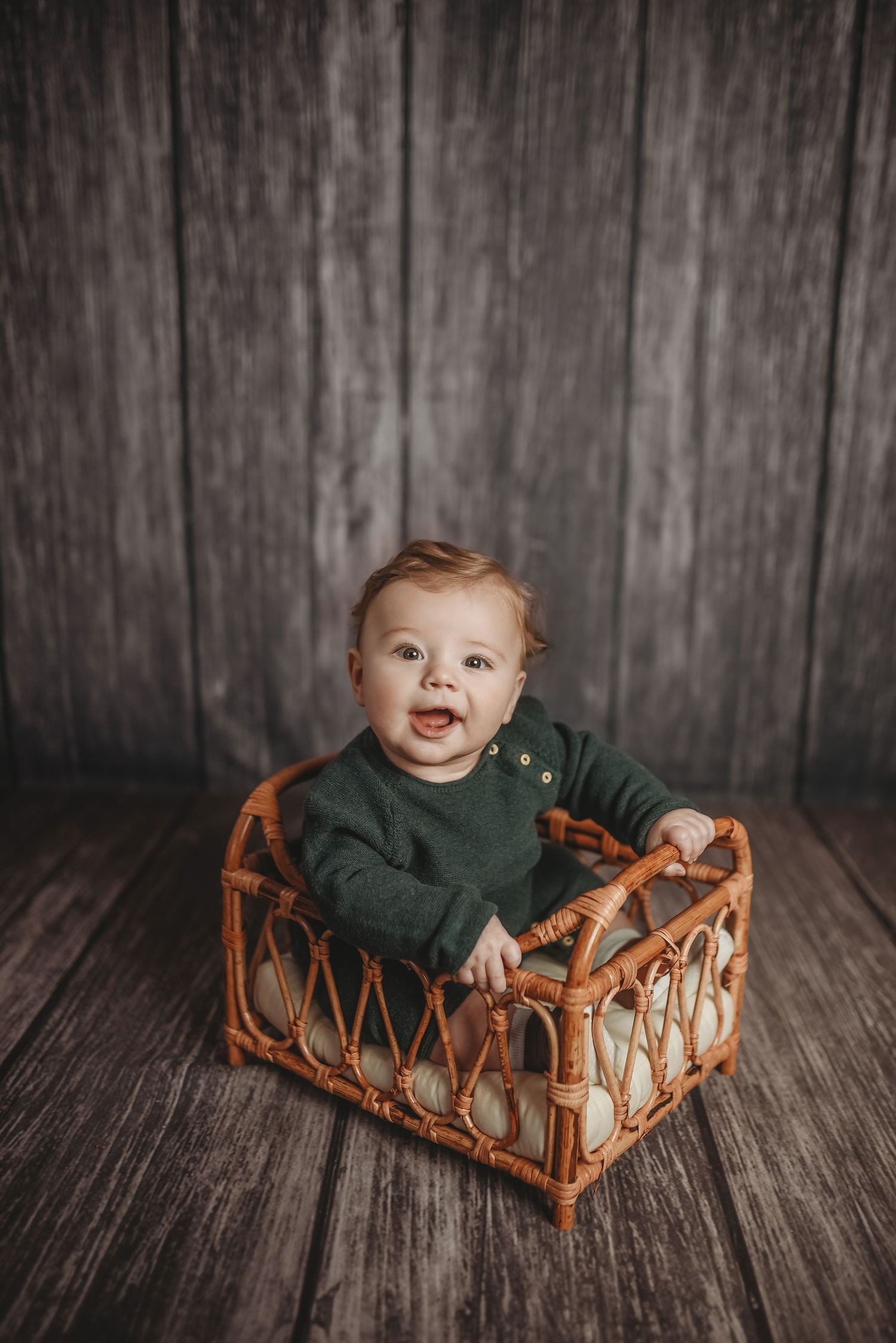 Baby photography session with rustic woven basket against gray wooden backdrop.