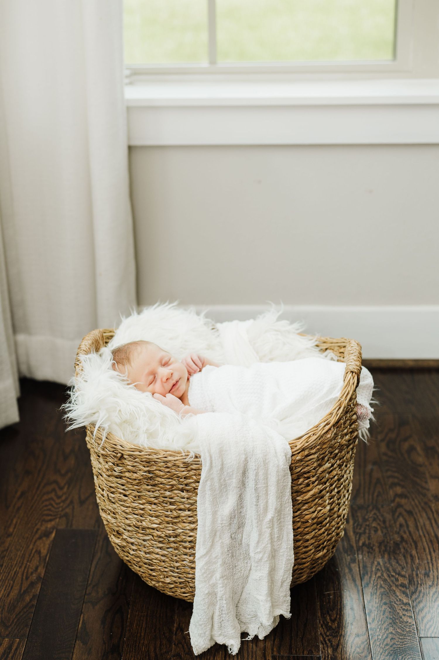 Sleeping newborn in cozy woven basket with white fabric draped across.