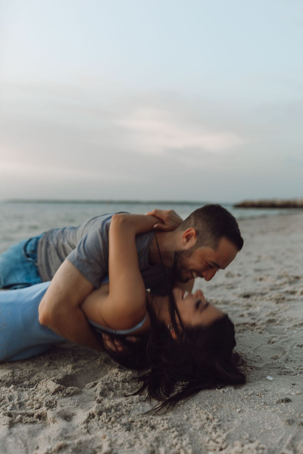 Beach engagement photo couple by the rocks and the ocean at sunset