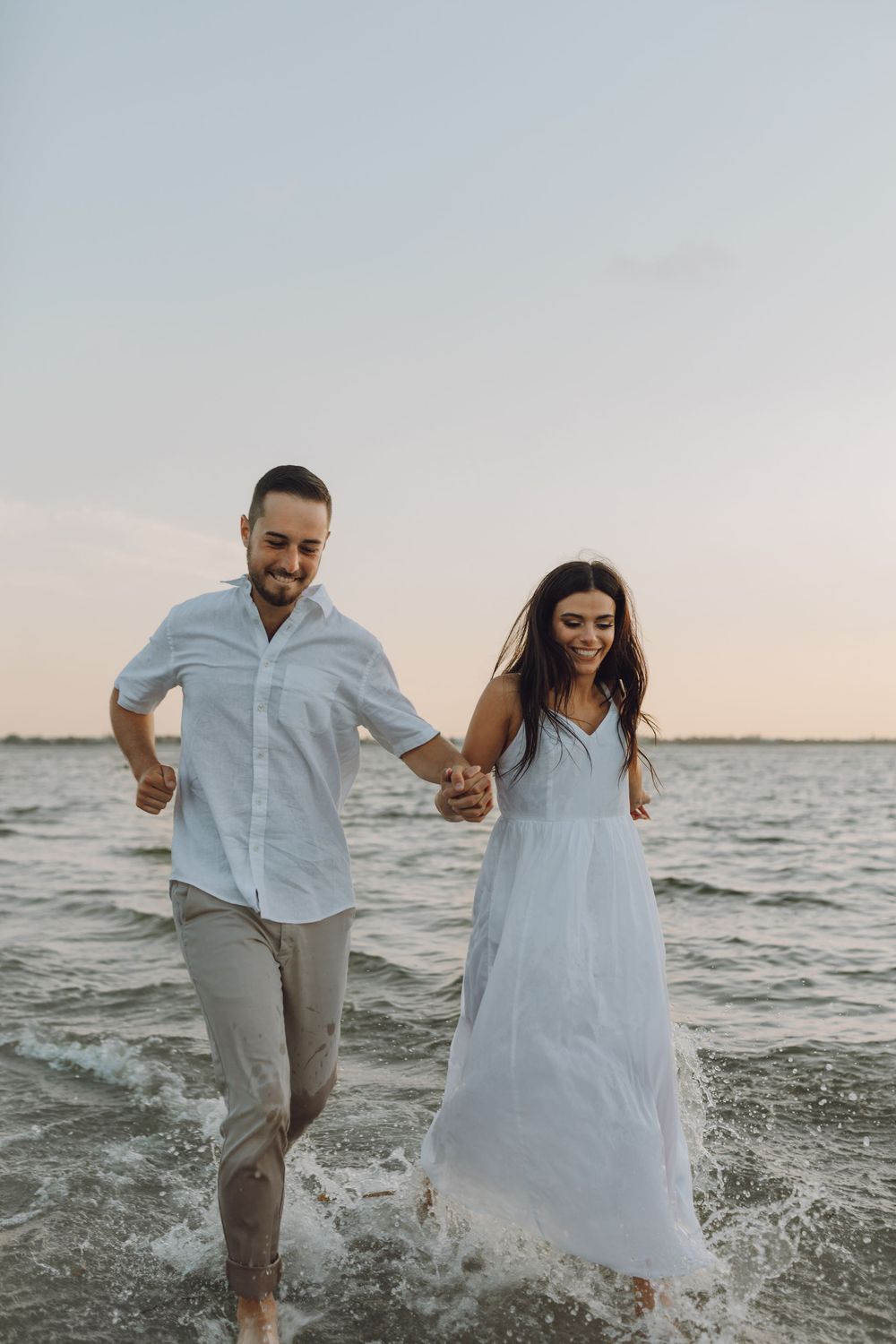 Beach engagement photo couple by the rocks and the ocean at sunset  with their dog