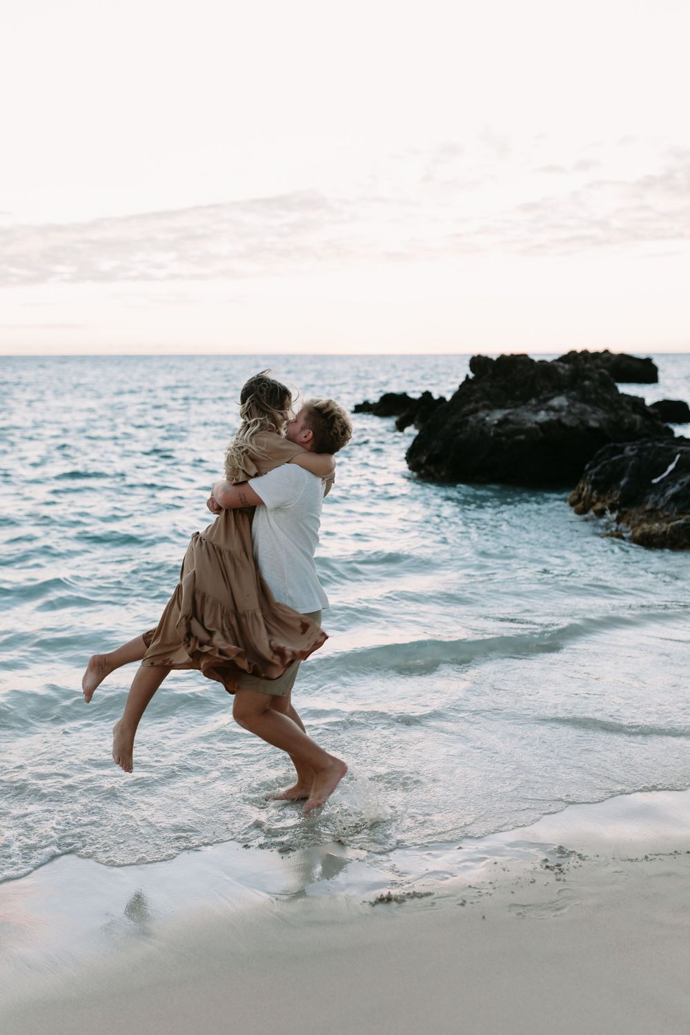 Beach couple photo in hawaii photographer by the ocean with rocks and sunset in the back