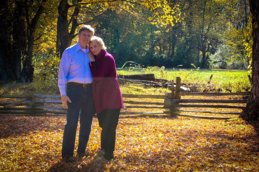 A couple embracing in a sunlit autumn forest with fallen leaves.