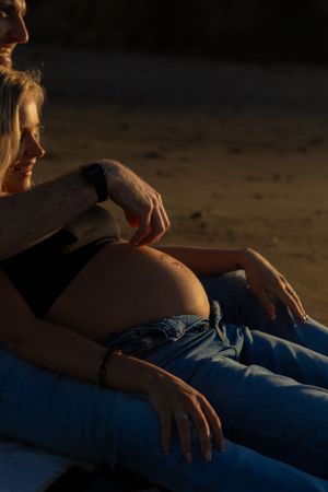 dark exposure detail image of beach maternity session, dad to be running fingers down the bump while sitting on the sand