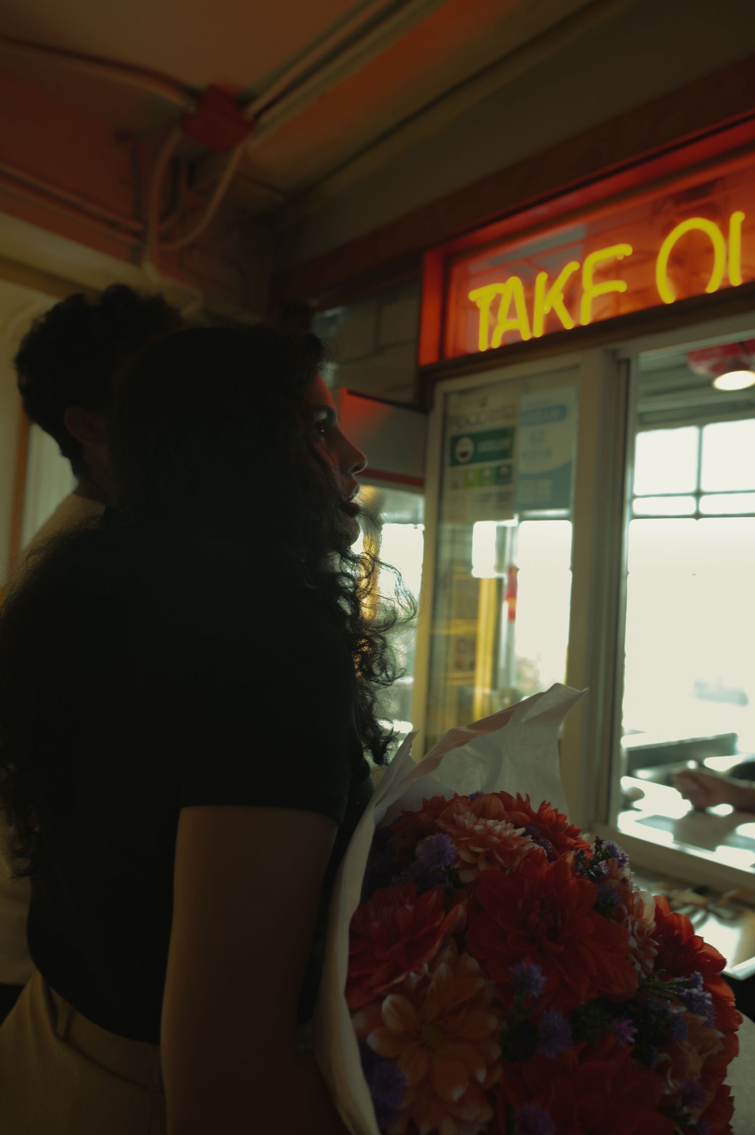 Silhouette of person standing beneath glowing red neon 'TAKE OUT' sign.