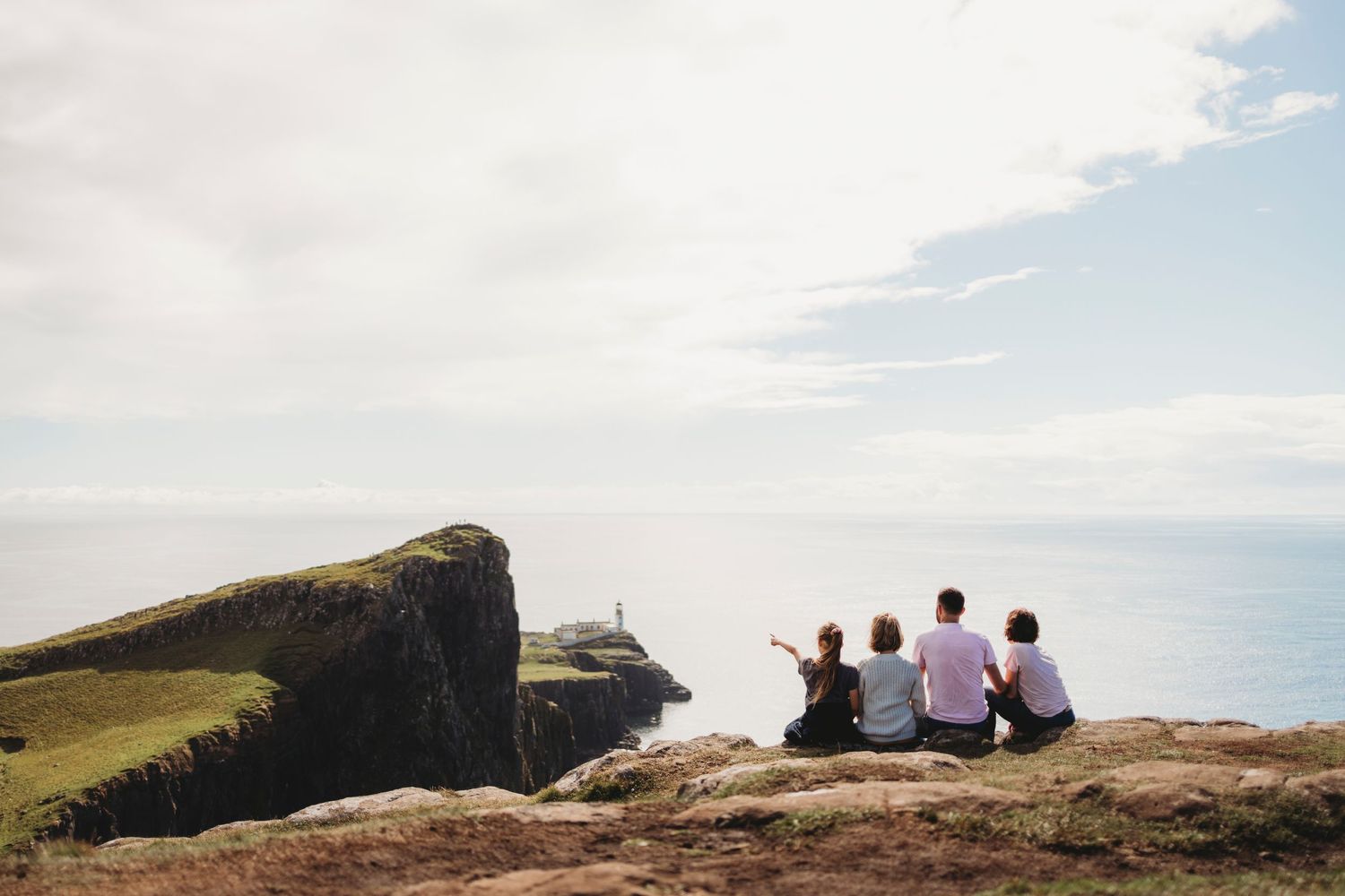 Group sitting together on cliff edge overlooking coastal scenery.