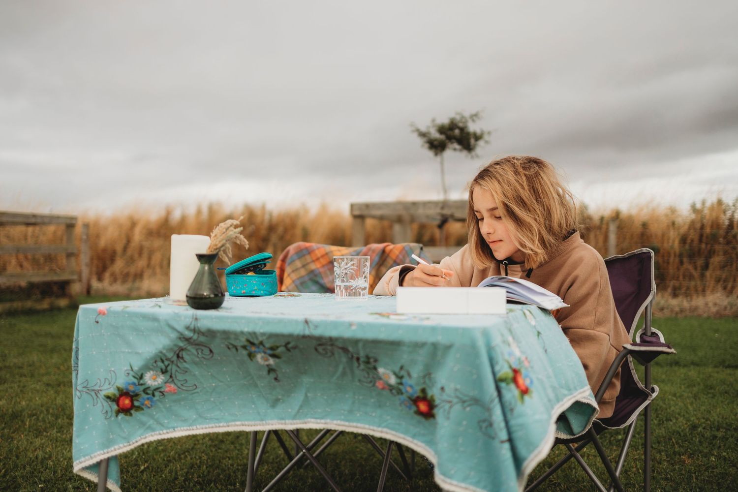 A person writes at a table decorated with a turquoise tablecloth outdoors.