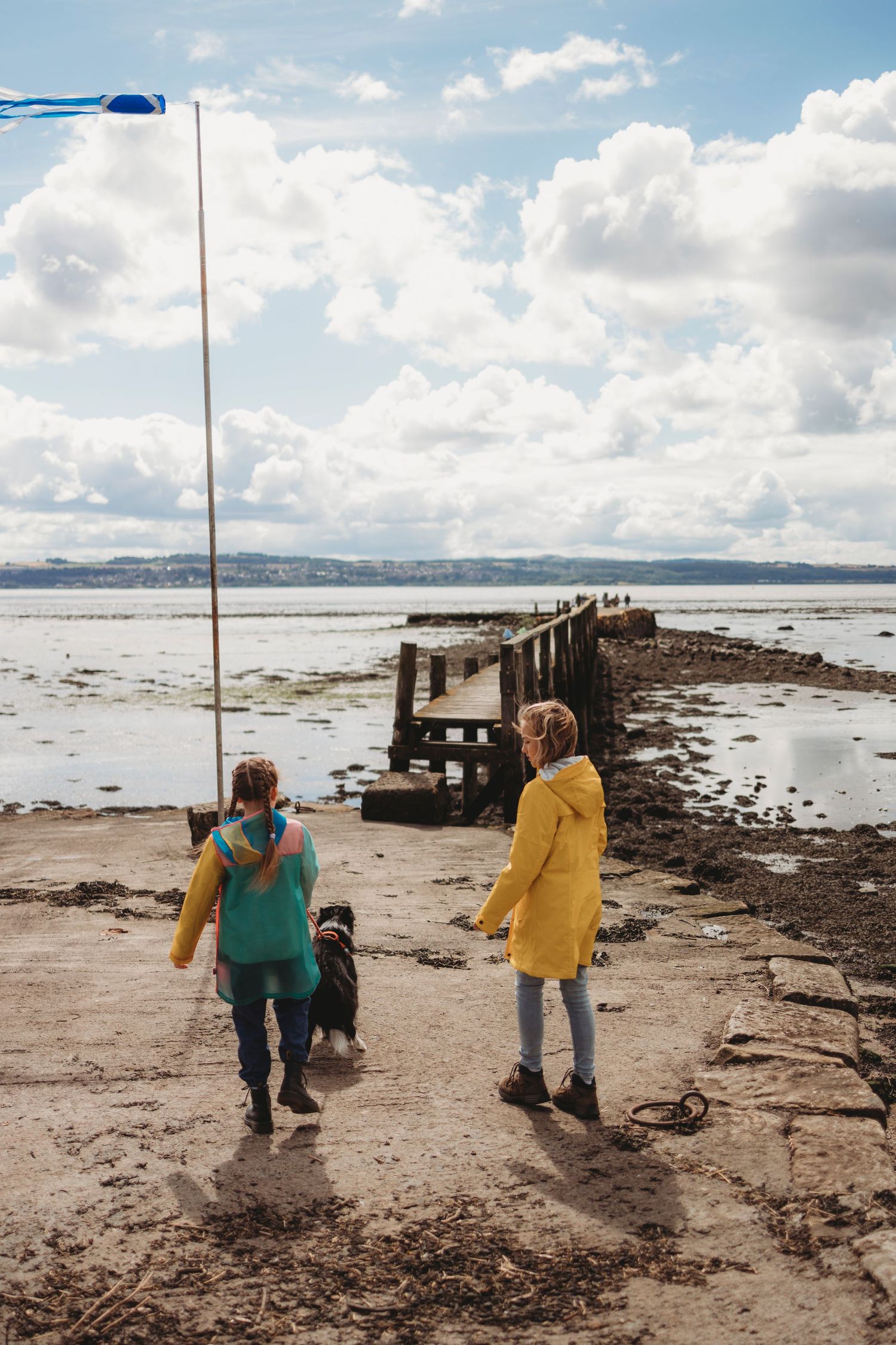 Two people in colorful coats walk with a dog on a coastal pier.