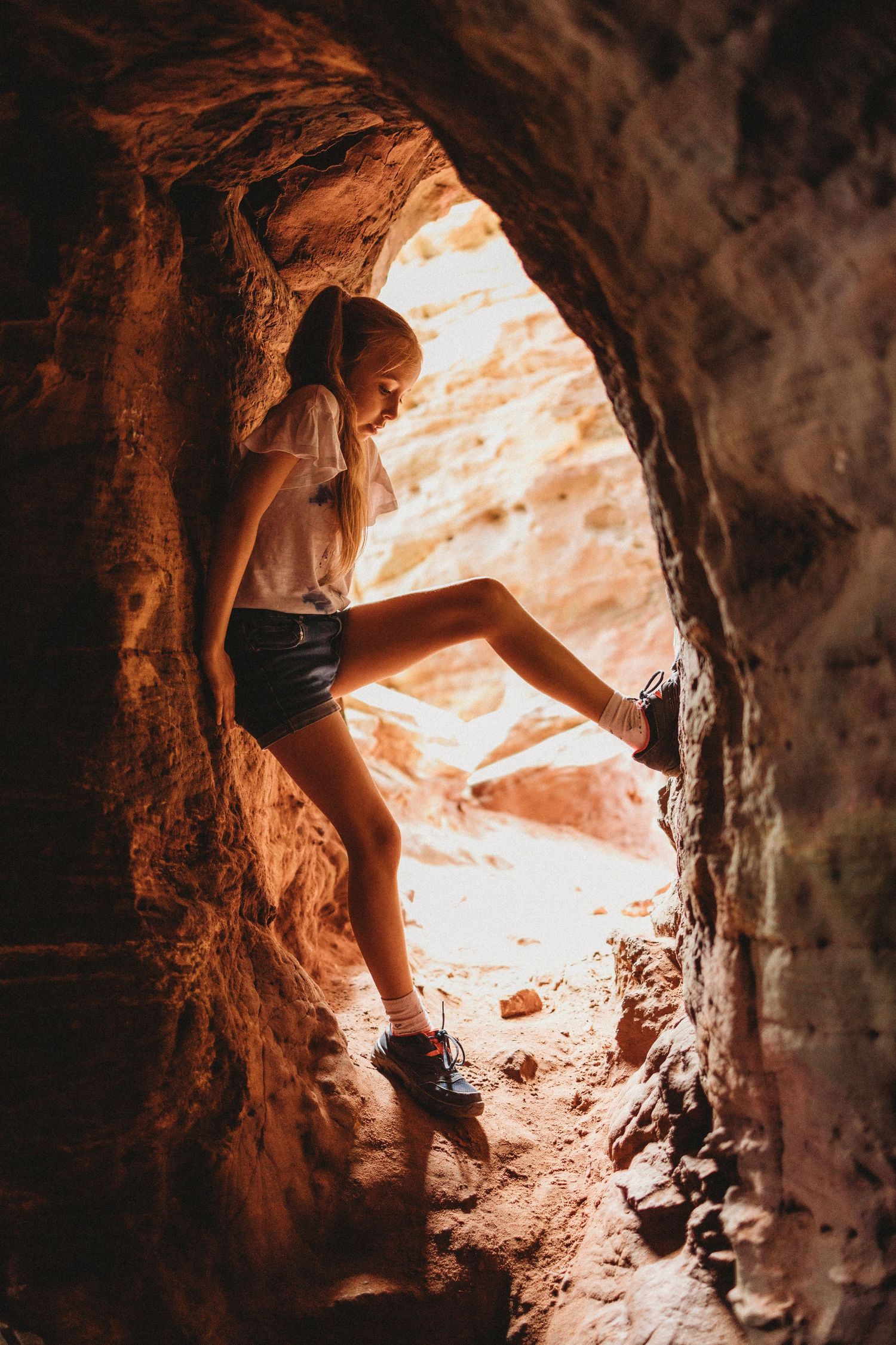 A silhouette explores a natural cave opening with warm sunlight streaming in.