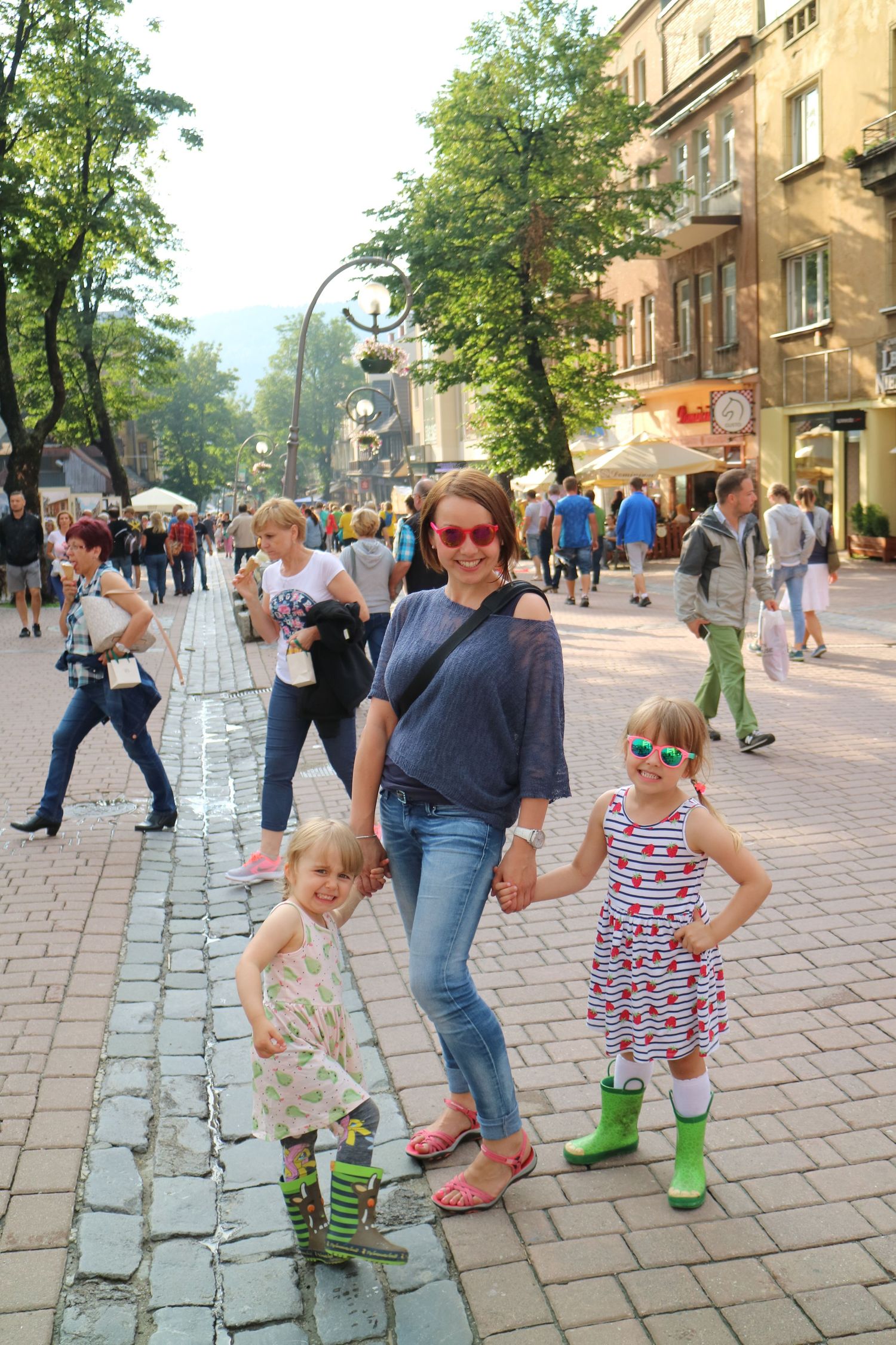 People walking along a busy European cobblestone street lined with historic buildings.