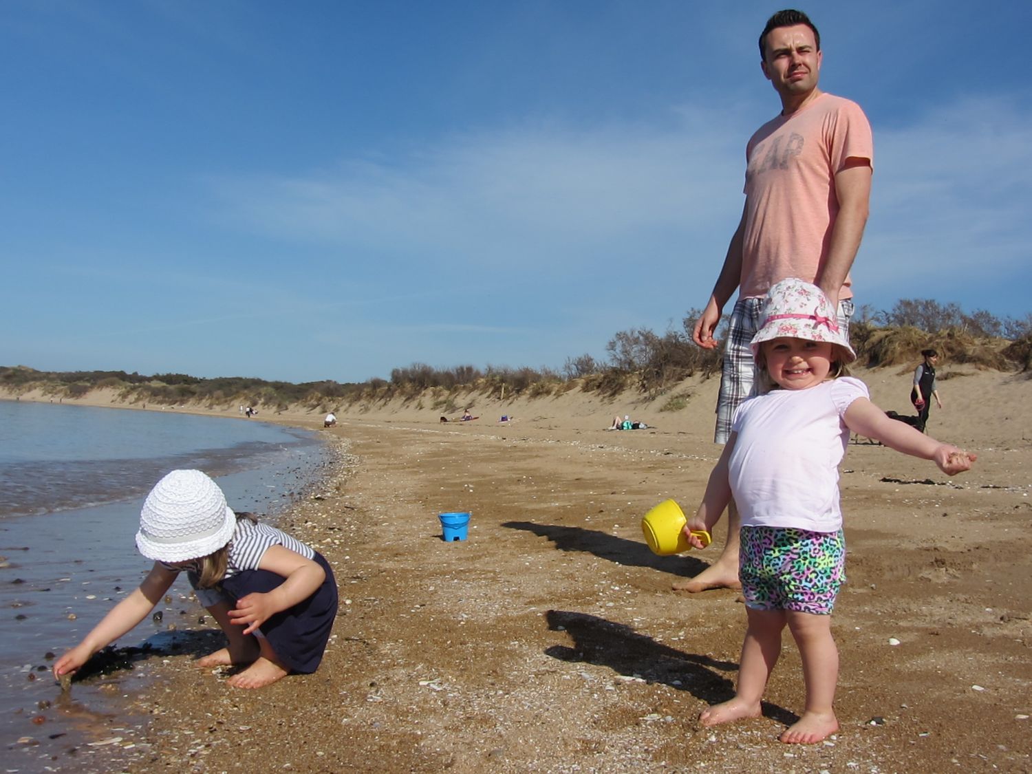 People playing and exploring on a sandy beach with dunes on a sunny day.