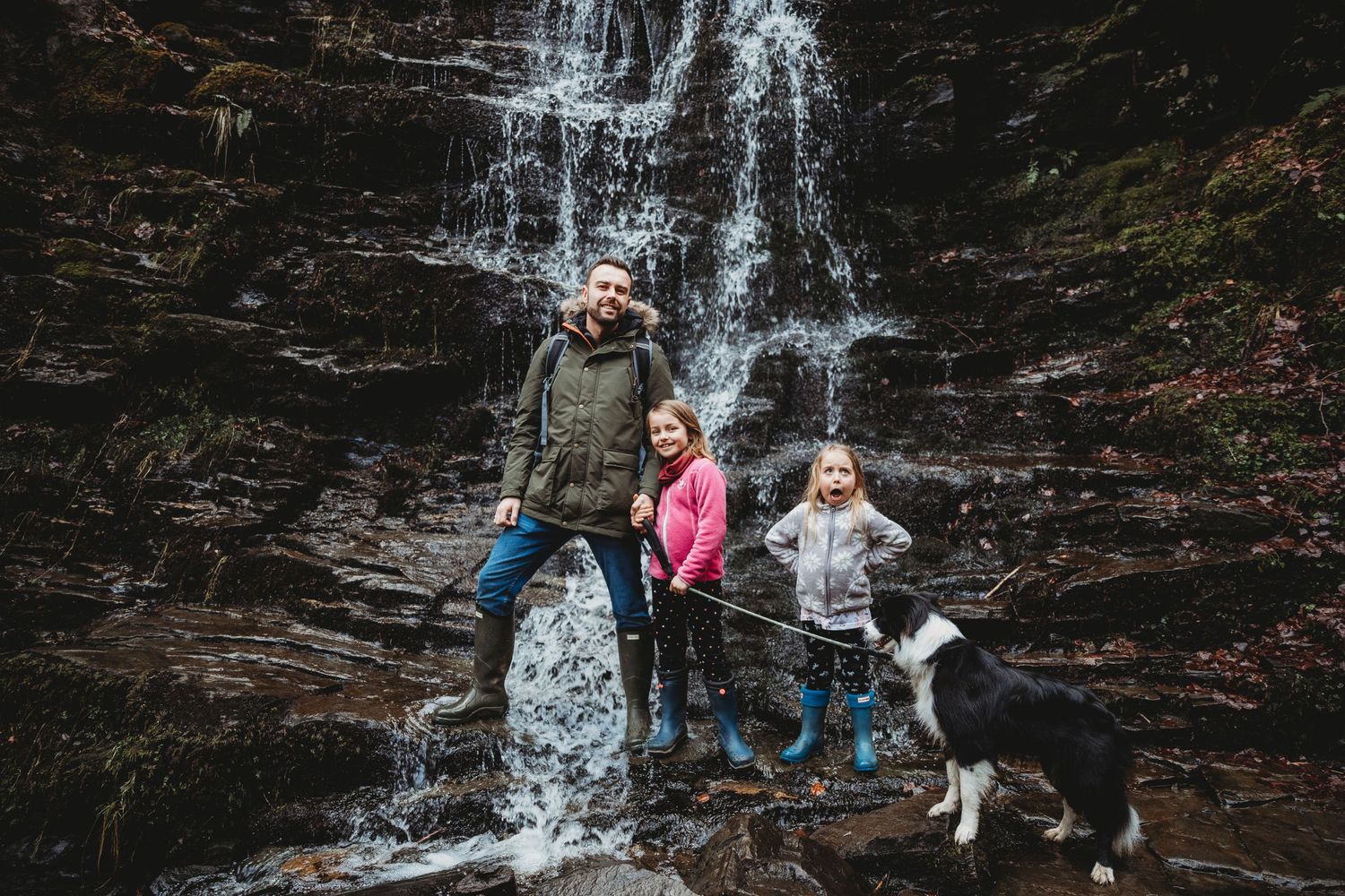 Group explores a scenic waterfall cascading down rocky cliffs with a dog companion.