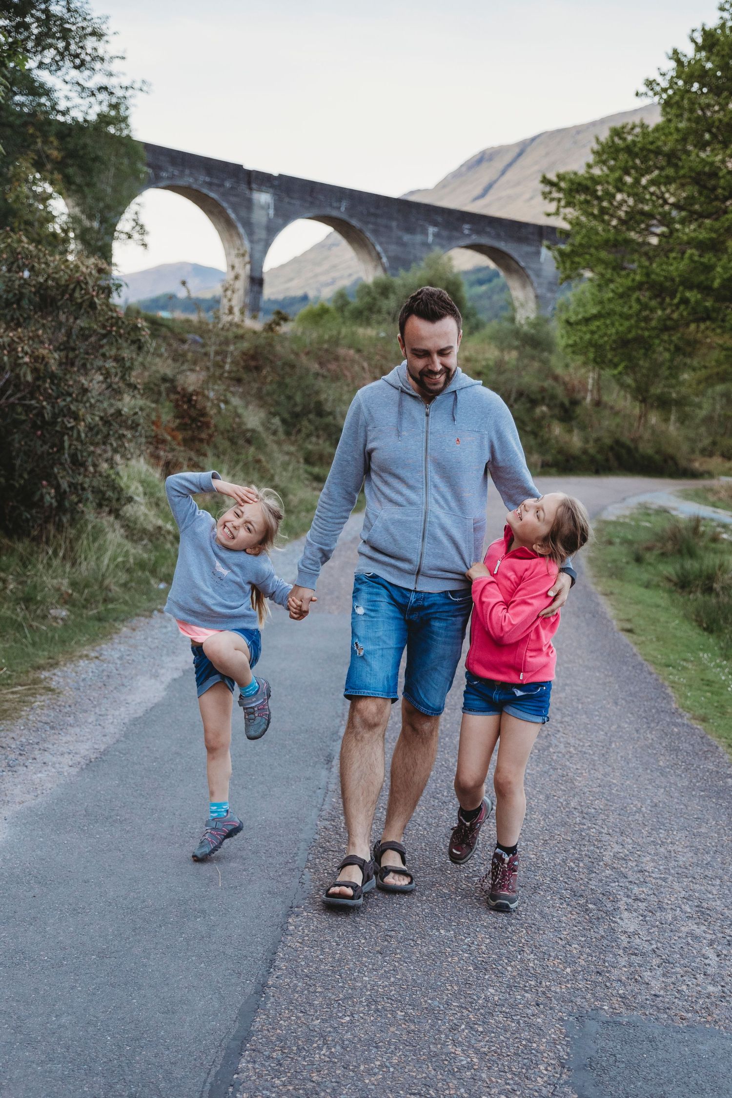 Walking together on a path beneath a historic stone railway viaduct in scenic countryside.